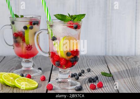 Frische hausgemachte Sommercocktails mit Eis, Limette und Beeren in Gläsern mit Stroh, Copyspace. Stockfoto