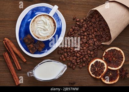 Tasse Kaffee mit cremefarbener Kaffeebohnen Schokolade und Gewürzen auf einem dunklen Holztisch. Weltkaffeetag Stockfoto