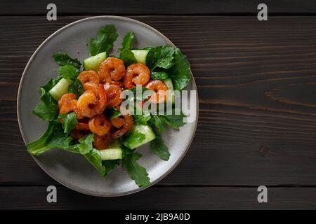 Frischer Salat mit gegrillten Garnelen, Gurken und Rucola, wunderschön auf einem Teller serviert, Draufsicht, flach liegend. Stockfoto