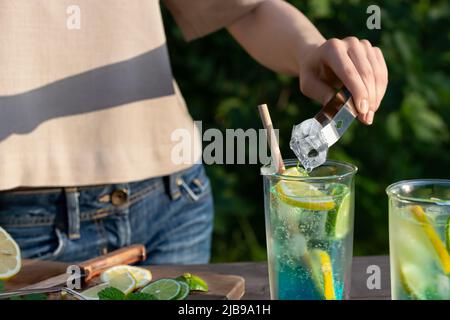 Mädchen macht Sommer erfrischende Cocktails blaue Lagune. Nahaufnahme des Einfügens von Eiswürfeln in Gläser. Selektiver Fokus. Stockfoto