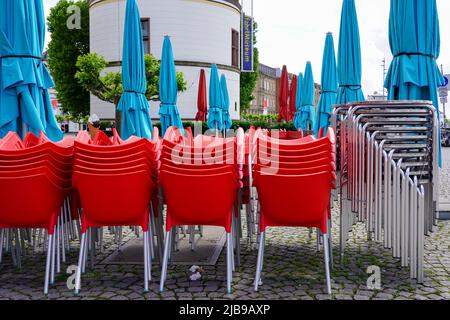 Gefaltete türkisfarbene Sonnenschirme und rote Bistrostühle übereinander auf dem Burgplatz vor dem Schifffahrtsmuseum. Düsseldorf, 23.5.33 Stockfoto