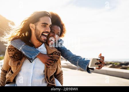 Glückliches multirassisches Paar, das Spaß hat, Selfie mit dem mobilen Smartphone während des Urlaubs zu machen - Jugendliche lieben und soziales Beziehungskonzept Stockfoto