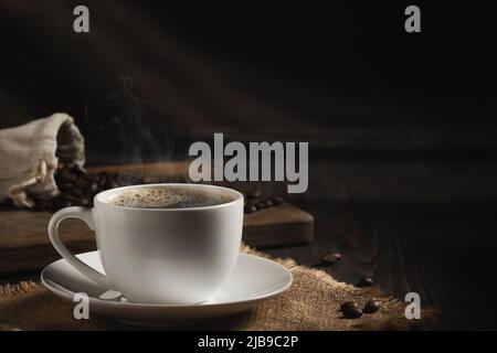 Weiße Tasse frischen heißen Kaffee und Kaffeebohnen auf Holzbrett auf dem Tisch, Copyspace. Stockfoto