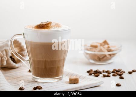 Latte-Kaffee, der in Schichten mit Schaum und einer knusprigen Schokoladenplatte auf einem hellen Küchentisch gegossen wird Stockfoto