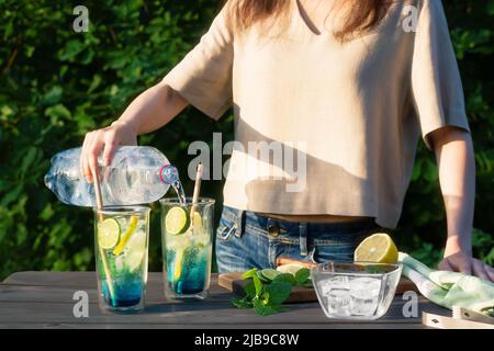 Mädchen macht Sommer erfrischende Cocktails blaue Lagune. Prozess des Gießens von Wasser in Gläser.Selektiver Fokus. Stockfoto