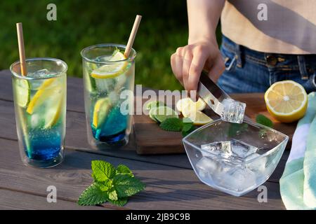 Mädchen macht Sommer erfrischende Cocktails blaue Lagune. Nahaufnahme des Einfügens von Eiswürfeln in Gläser. Selektiver Fokus. Stockfoto