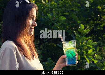 Eine junge Frau mit langen dunklen Haaren hält einen erfrischenden Cocktail in der Hand. Selektiver Fokus. Stockfoto