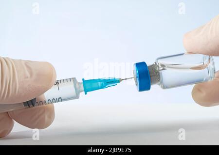 Impfstoff im Fläschchen mit punktierte Spritze auf blauem Hintergrund Stockfoto