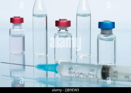 Glasfläschchen mit Flüssigkeit, einem Impfstoff und einer medizinischen Spritze in Nahaufnahme auf blauem Hintergrund. Das Konzept der Impfung gegen Coronavirus . Banner, Kopie sp Stockfoto