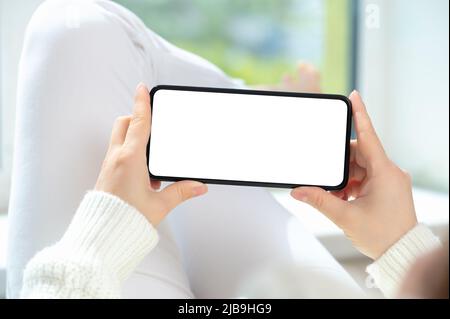 Frau liegt in entspannter Position und sieht sich Videoinhalte an oder spielt Spiele auf dem Handy oder Smartphone. Handy zu Hause mockup Stockfoto
