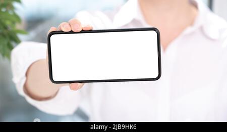 Handy-Mockup. Frau in weißer Kleidung zeigt leeren weißen Handy-Bildschirm in horizontaler Position. Frau Hand hält und zeigt schwarze Handy smart Stockfoto