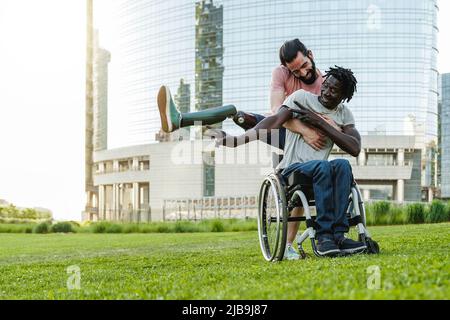 Glückliche, vielfältige Freunde mit Behinderung, die im Stadtpark Spaß haben - Fokus auf afrikanischen Mann im Rollstuhl Stockfoto