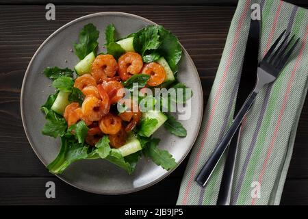 Frischer Salat mit gegrillten Garnelen, Gurken und Rucola, wunderschön auf einem Teller serviert, Draufsicht, flach liegend. Stockfoto