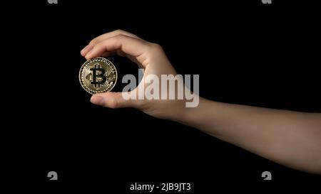 Die Hand der Frau hält eine Bitcoin in ihren Fingern. Isoliert auf schwarzem Hintergrund. Stockfoto