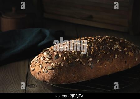 Laib hausgemachtes Vollkornbrot mit Samen kühlen sich auf einem Drahtgestell auf einem Holztisch ab. Stockfoto