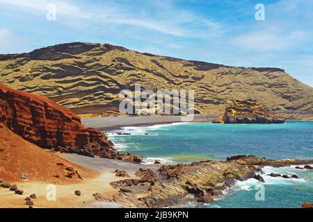 Wunderschöne, abgeschiedene Lagune, umgeben von beeindruckenden, zerklüfteten, verwitterten Klippen, verschiedenen Farben, roten Felsen, leerstem, schwarzen Sandstrand - El Golfo, La Stockfoto