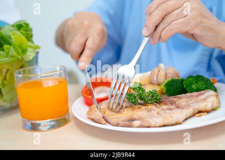 Asiatische ältere oder ältere alte Dame Frau Patientin essen Frühstück und Gemüse gesunde Lebensmittel mit Hoffnung und glücklich, während sitzen und hungrig auf dem Bett in der Zusammenarbeit Stockfoto