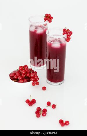 Roter Johannisbeersaft in zwei hohen Gläsern. In einer kleinen weißen Schale daneben stehen rote Johannisbeeren. Stockfoto