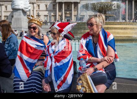 Drei Frauen, die in Unionsflaggen gehüllt sind, sitzen am Trafalgar Square in London während der Feierlichkeiten zum Platin-Jubiläum der Königin am 2. Juni 2022 Stockfoto