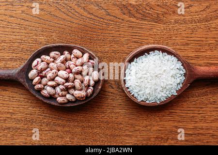 Weißer Reis und Pinto-Bohnen auf hölzernen Küchenlöffeln. Brauner, hölzerner Hintergrund. Glutenfreie, gesunde Lebensmittel Stockfoto