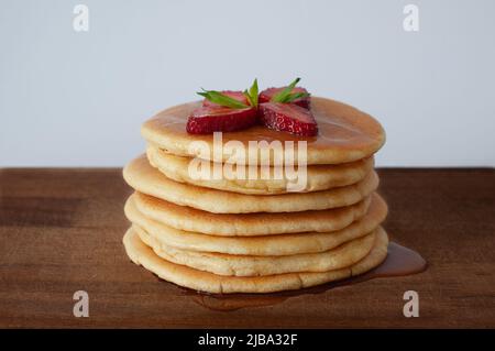 Köstliche hausgemachte Pfannkuchen mit Nahaufnahme und selektivem Fokus. Erdbeeren und Ahornsirup auf dem Stapel. Isoliert auf weißem Hintergrund. Stockfoto