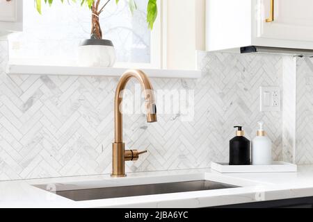 Waschbecken Detail in einer luxuriösen Küche mit Fischgrät backsplash Fliesen geschossen. Weißen Marmor Arbeitsplatte und Gold Wasserhahn. Stockfoto