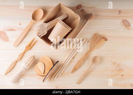 Verschiedene Küchenutensilien auf einem Holztisch. Set aus Holzbesteck und biologisch abbaubaren Pappbecher aus Karton. Umweltfreundlicher, nachhaltiger Lebensstil. Keine Wa Stockfoto