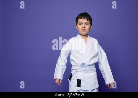 Porträt eines charmanten selbstbewussten Aikido-Wrestlers - kaukasischer Teenager in weißem Kimono isoliert auf violettem Hintergrund mit Platz für Werbetexte Stockfoto