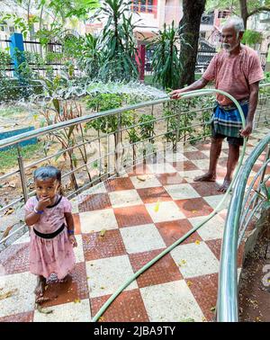 Chennai, Indien, 4.. Juni 2022: Ein Gärtner (Großvater), der die Pflanzen in einem Park wässert, während seine Enkelin den Nieselregen genießt, der die Hitze in Chennai schlägt. Seshadri Sukumar Stockfoto