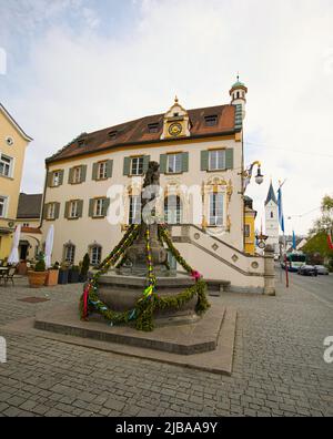 Fürstenfeldbruck, Bayern, Deutschland - 23. April 2022: Geschmückter Kriegerbrunnen und altes Rathaus mit St. Leonhard Kirche im Hintergrund. Stockfoto