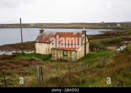 Ein älteres und baufällig gewelltes Häuschen mit Steinstapeln im Hafen von Berneray, jenseits von North Uist in den Äußeren Hebriden, Schottland Stockfoto