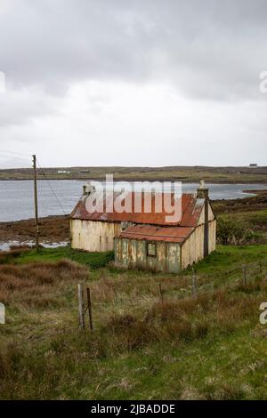 Ein älteres und baufällig gewelltes Häuschen mit Steinstapeln im Hafen von Berneray, jenseits von North Uist in den Äußeren Hebriden, Schottland Stockfoto