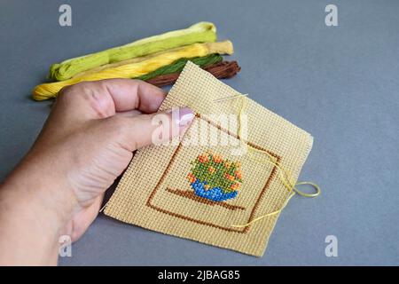 Nahaufnahme der Frauenhand, die Kreuzstich auf hellbraunem Baumwolltuch macht. Handgemachte Stickerei, Satz von bunten Fäden. Selektiver Fokus. Kopie sp Stockfoto