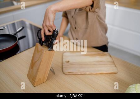 Eine unkenntliche Frau zieht ein Küchenmesser aus dem Block, bevor sie mit dem Kochen beginnt Stockfoto