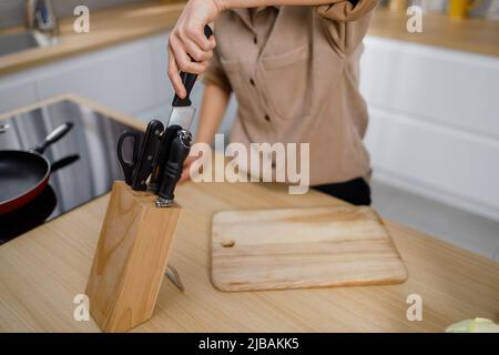 Messer im Holzblock in der Küche. Die Frau wählt das richtige Messer aus dem Set Stockfoto