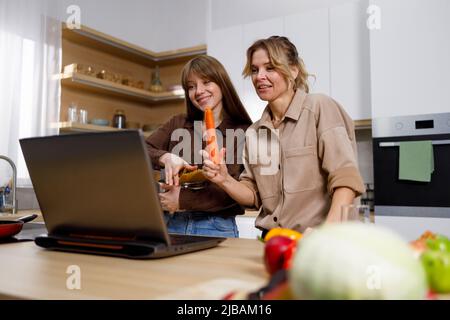 Mutter und Erwachsene Tochter kochen zusammen und betrachten den Laptop Stockfoto
