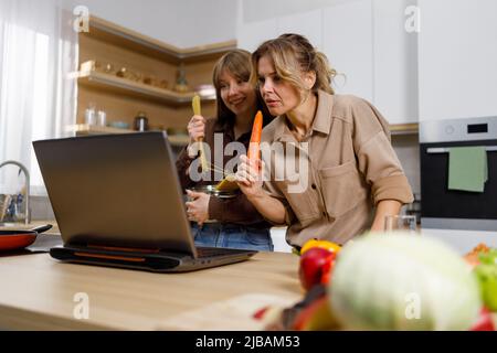 Frau und ihre Erwachsene Tochter kochen gemeinsam in der Küche nach einem Rezept aus dem Internet Stockfoto