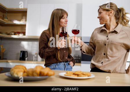 Die Erwachsene Tochter und ihre attraktive Mutter trinken Rotwein in der Küche und reden Stockfoto