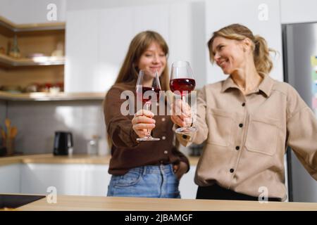 Zwei Frauen unterschiedlichen Alters in der Küche klirken Gläser mit Rotwein Stockfoto