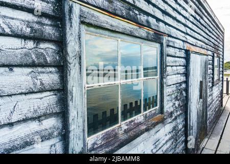 Lagunenspiegelungen im Fenster von alten Holzwharf und Schuppen auf Lagune in der kleinen Stadt Okarito, Westland, Neuseeland. Stockfoto