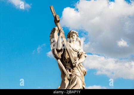 Eine Steinstatue eines Engels mit Flügeln, die ein heiliges Kreuz in Rom, Italien, mit einem blauen Himmel Hintergrund halten. Ponte Sant'Angelo die Engelsbrücke. Stockfoto