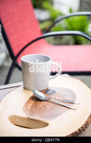 Eine Tasse Tee oder Kaffee auf einem Holztisch mit Holzkaffee auf der Terrasse eines Hotels oder einer Air BnB-Einheit. Stockfoto