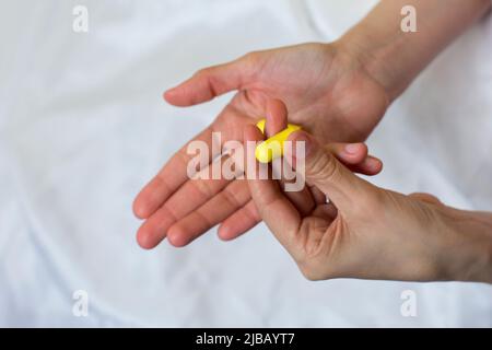 Nahaufnahme der weiblichen Hände und der gelben Schaumstoffohrstöpsel. Frau, die den antinoise-Ohrstöpsel nimmt. Heller Hintergrund. Stockfoto