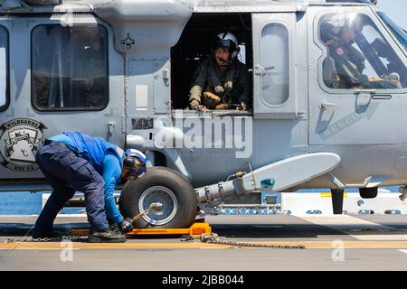 220603-N-CM110-1029 PAZIFISCHER OZEAN, Japan (3. Juni 2022) – der Flugzeugflieger Timothy Rodriguez von Aviation Boatswain aus Houston kettet und kettet einen Hubschrauber MH-60s Sea Hawk, der dem Hubschrauber Sea Combat Squadron (HSC) 23 zum Flugdeck an Bord des amphibischen Angriffsträgers USS Tripoli (LHA 7) zugewiesen wurde, 3. Juni 2022. Tripolis führt Routineoperationen in der US 7.-Flotte durch. (USA Navy Foto von Mass Communication Specialist 3. Class Maci Sternod) Stockfoto