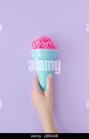 Frau Hand halten rosa Papier Eis Schaufel mit Eis Kunststoff-Kegel auf pastelllila Hintergrund. Minimales Sommerkonzept. Mikroplastik in Lebensmitteln Stockfoto