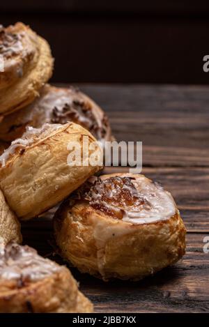 Hausgemachte, glasierte Blätterteig-Zimtrollen mit Pudding und Rosinen auf Holzboden. Stockfoto