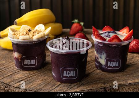Mix aus köstlichen brasilianischen Açaí Creme, in einem Kunststoff-Cup mit einer Vielzahl von Belägen, in einem rustikalen Holzhintergrund. Sommer acai Smoothie Stockfoto