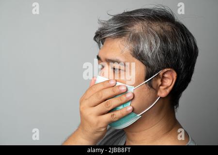 Kranker asiatischer Mann, der eine medizinische Gesichtsmaske trägt und hustet und seinen Mund mit meiner Hand bedeckt. Konzept zum Schutz des pandemischen Coronavirus und Atemschutzgeräts Stockfoto