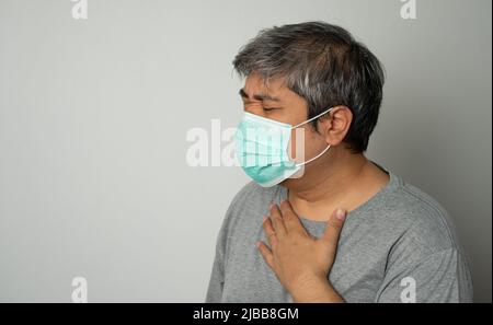 Kranker asiatischer Mann, der eine medizinische Gesichtsmaske trägt und hustet und seinen Mund mit meiner Hand bedeckt. Konzept zum Schutz des pandemischen Coronavirus und Atemschutzgeräts Stockfoto
