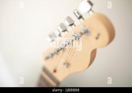 Holzhals einer E-Gitarre im Vordergrund mit ihren metallischen und verchromten Saiten und Stimmwirbel Stockfoto